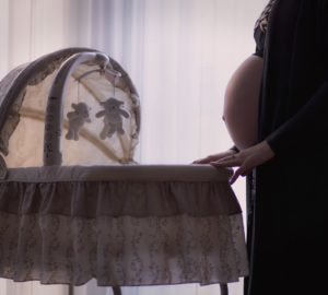 Kobieta z ciążowym brzuszkiem stoi nad niemowlęcą kołyską.